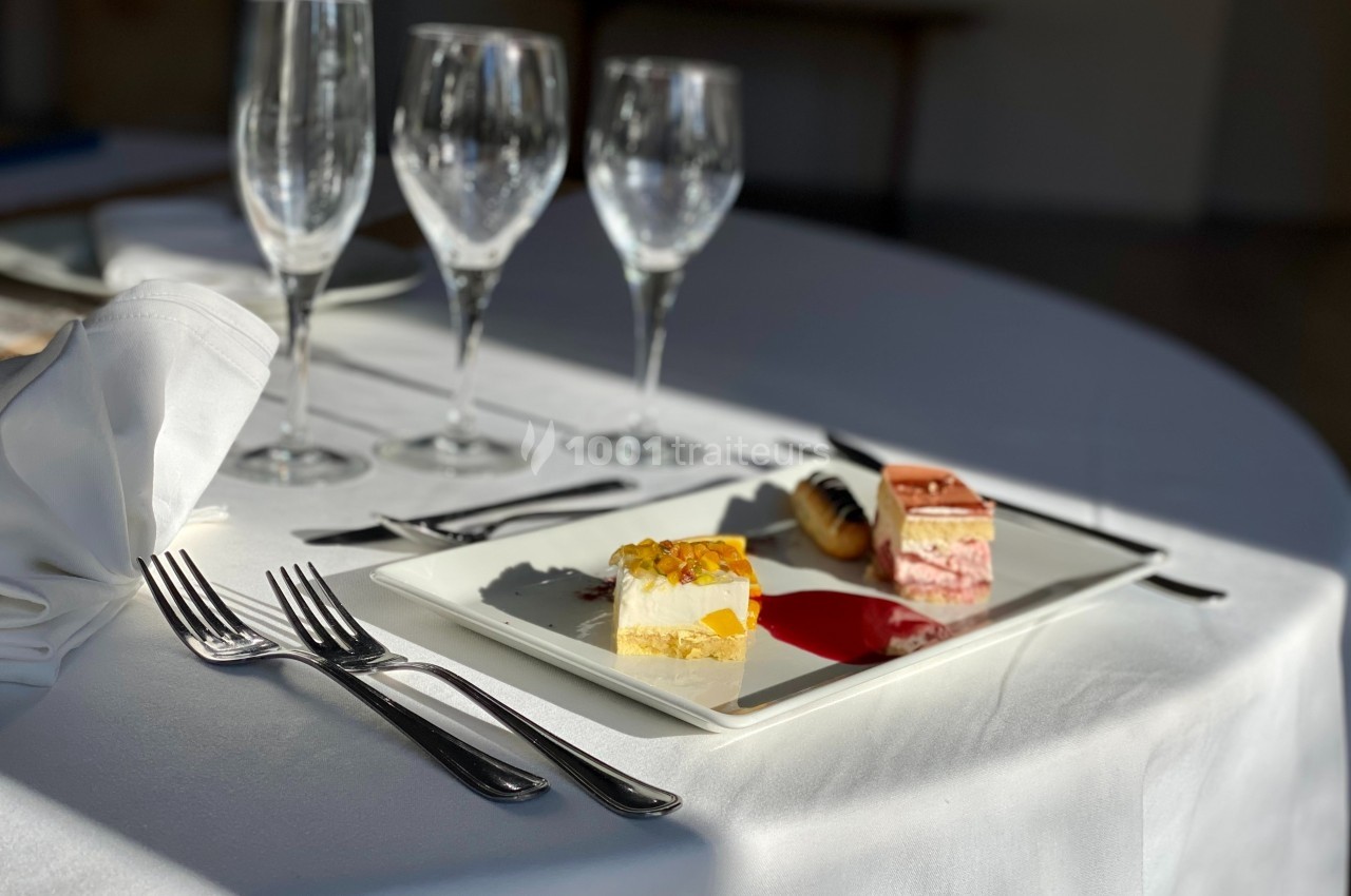 Assiette de desserts variés sur une table dressée avec des couverts et des verres à pied.