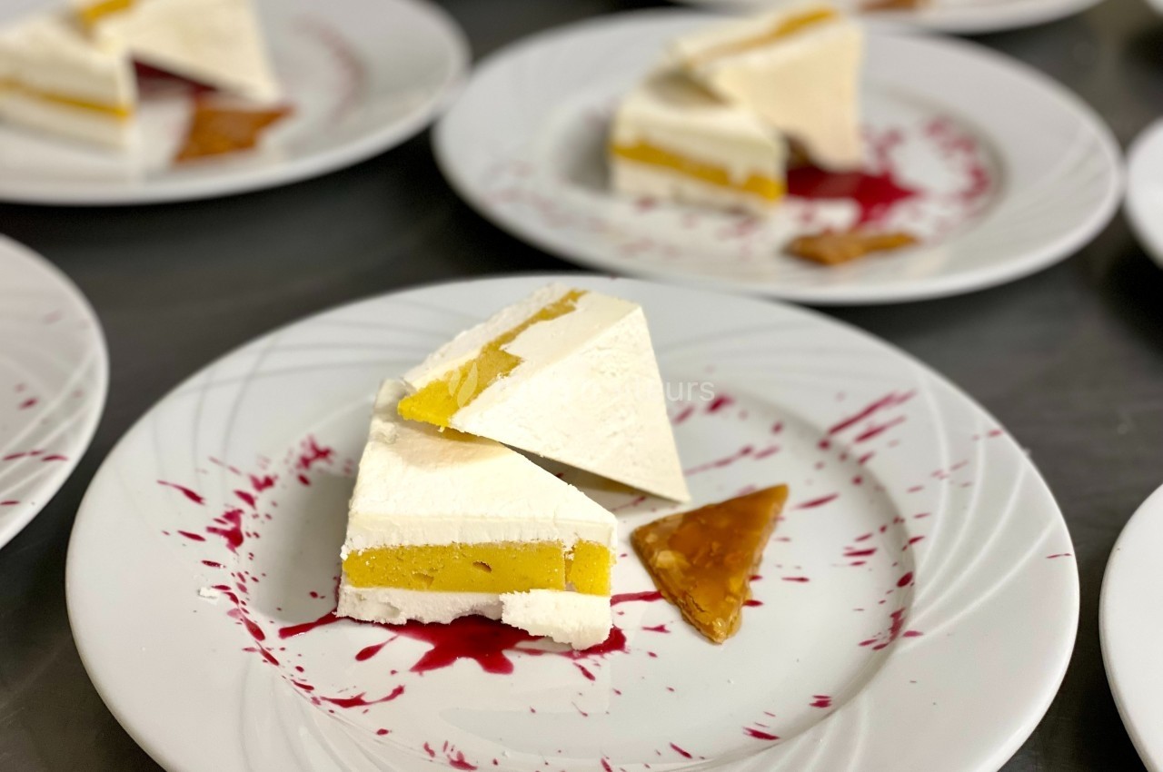 Part de dessert glacé à la mangue et à la crème, servie avec un coulis rouge et un éclat de caramel.