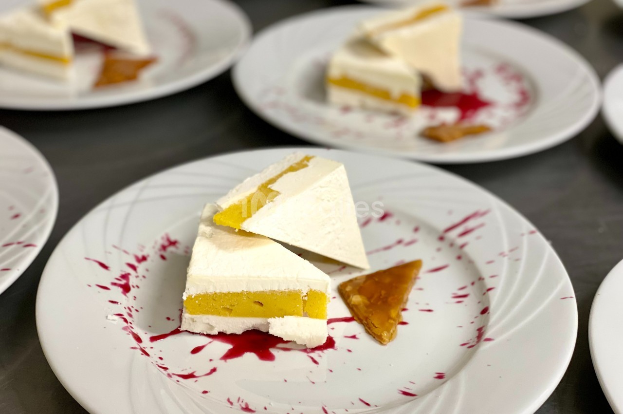 Part de dessert glacé à la mangue et à la crème, servie avec un coulis rouge et un éclat de caramel.