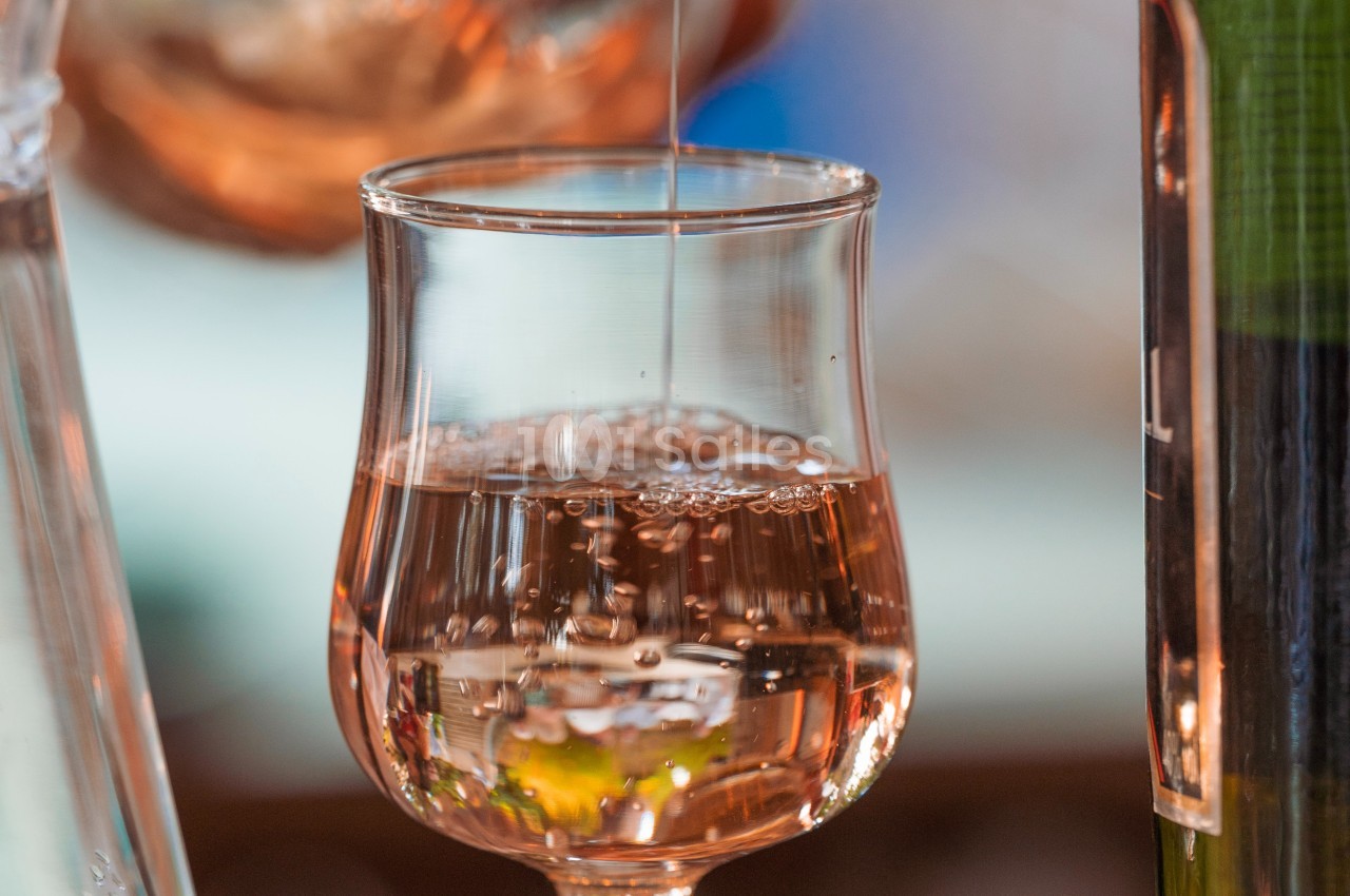 Verre de vin rosé en gros plan avec des reflets lumineux et un liquide en train d’être versé.