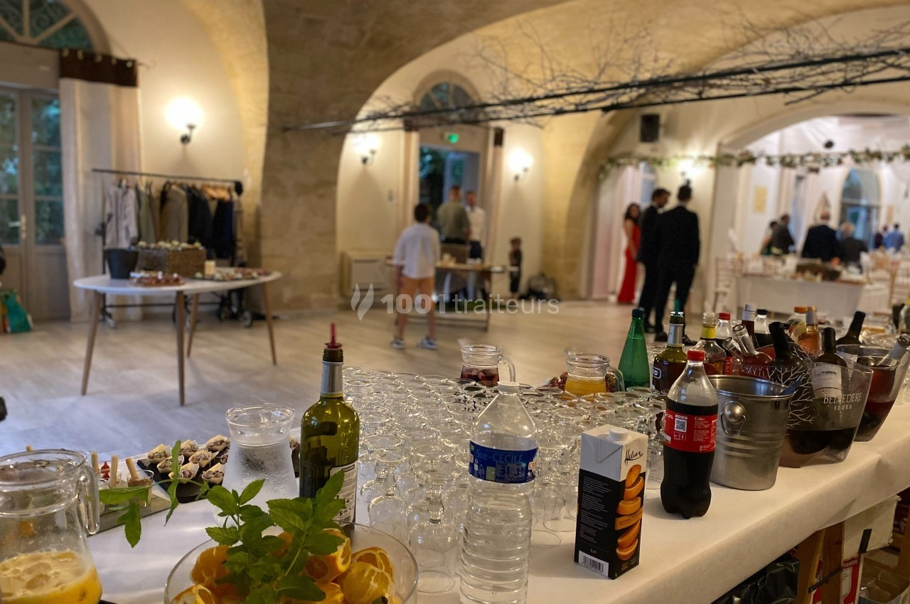 Table de boissons et apéritifs dans une salle de réception lumineuse avec des invités en arrière-plan.