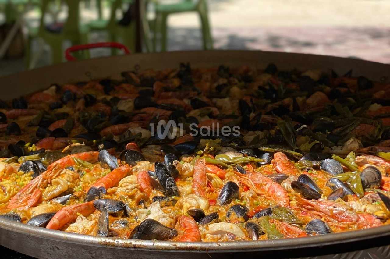 Grande poêle de paella garnie de fruits de mer, poulet, légumes et riz safrané, cuite en extérieur.