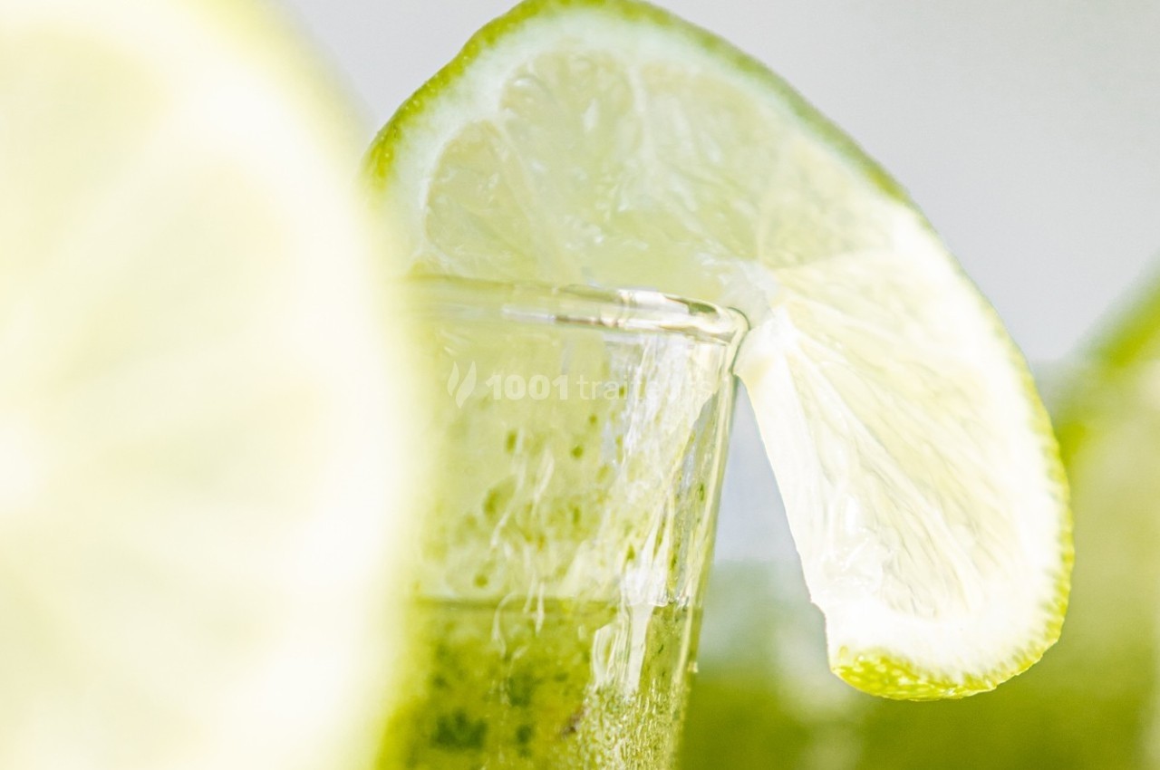 Tranche de citron vert posée sur le bord d'un verre contenant une boisson verte, avec un arrière-plan flou.