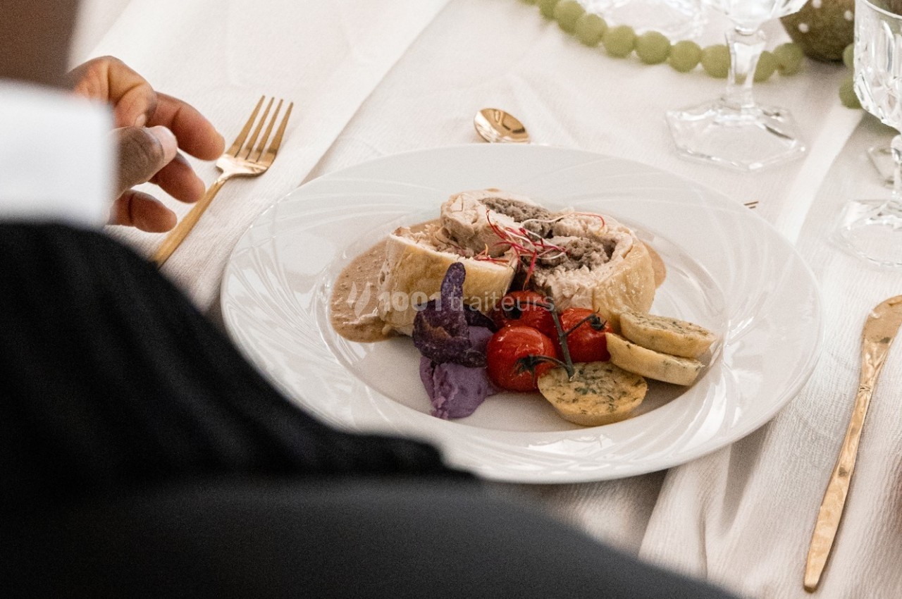 Assiette garnie de volaille farcie, légumes rôtis, chips violettes et accompagnements sur une table élégamment dressée.