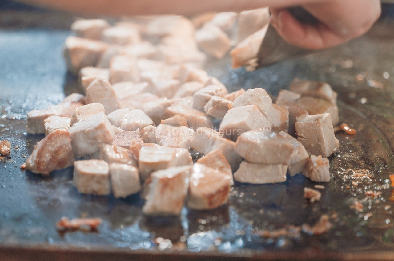 Morceaux de poulet en train de cuire sur une plaque chauffante, retournés à l'aide d'une spatule.