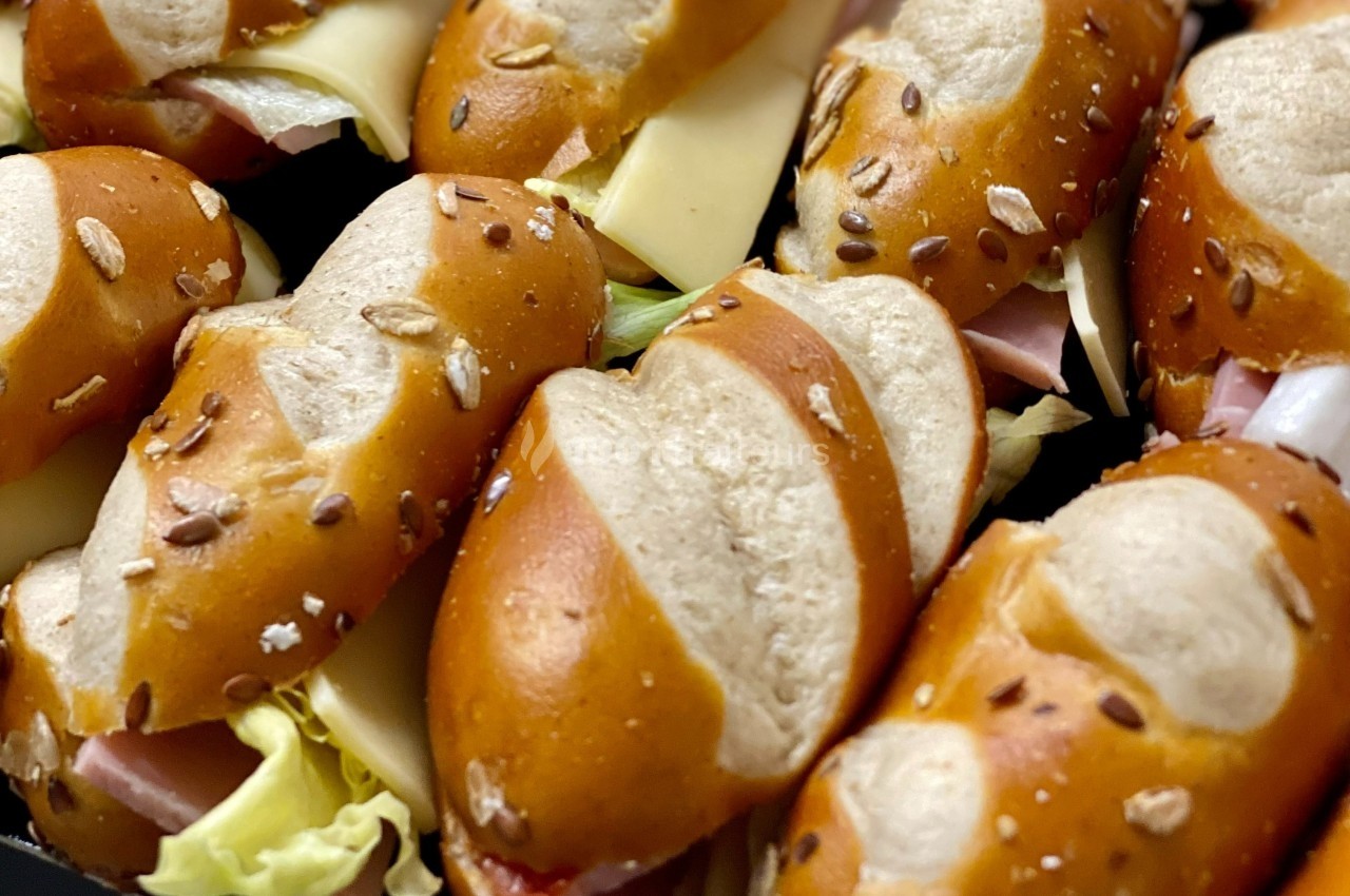 Petits sandwichs au pain bretzel garnis de fromage, jambon, laitue et graines sur le dessus.