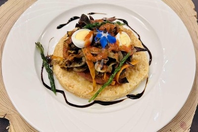 Plat gastronomique composé d'une mousse verte, surmontée de saumon et de pousses, présenté dans une assiette blanche.