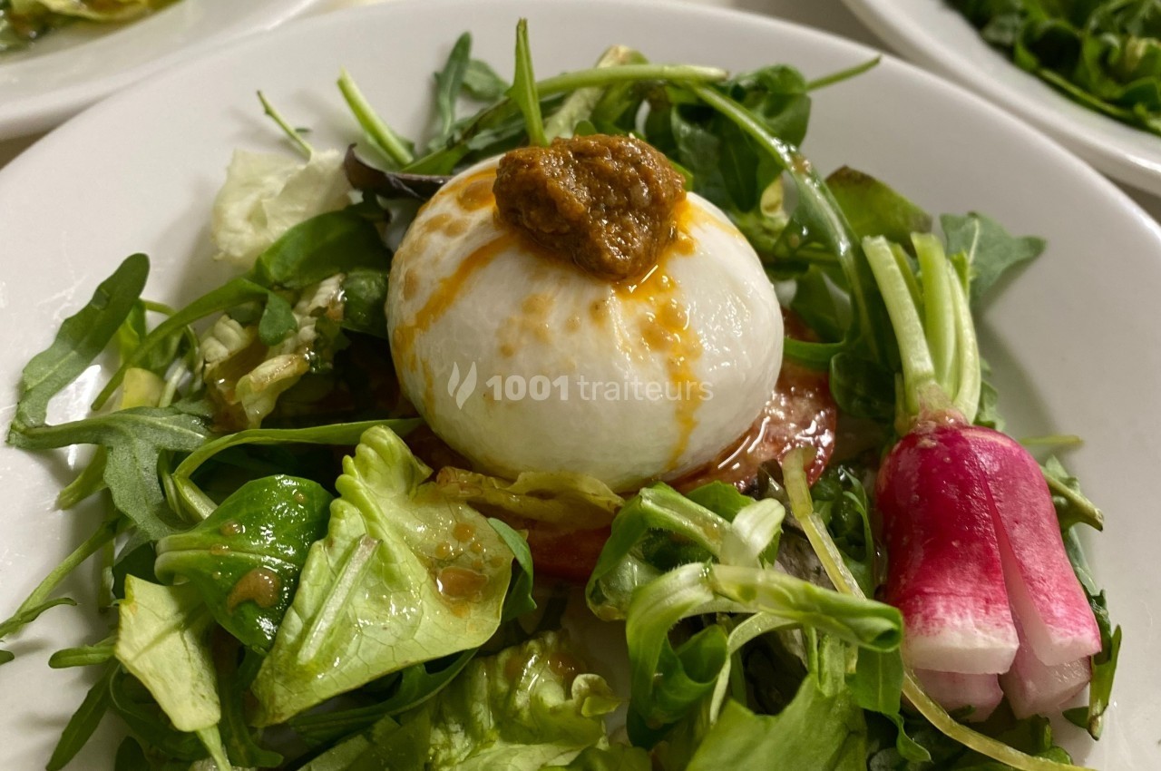 Assiette de salade composée avec burrata, roquette, radis et sauce, présentée sur un lit de légumes verts.