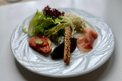 Plat gastronomique composé d'une mousse verte, surmontée de saumon et de pousses, présenté dans une assiette blanche.