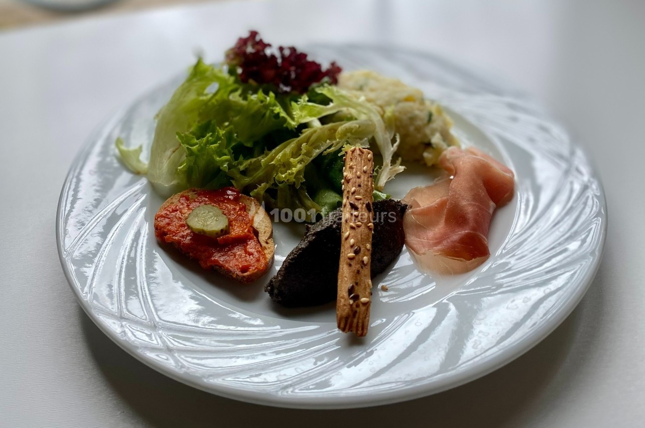 Assiette contenant de la salade verte, du jambon cru, un toast garni, une tapenade et un biscuit salé.