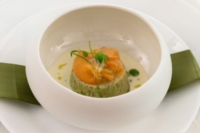 Plat gastronomique composé d'une mousse verte, surmontée de saumon et de pousses, présenté dans une assiette blanche.