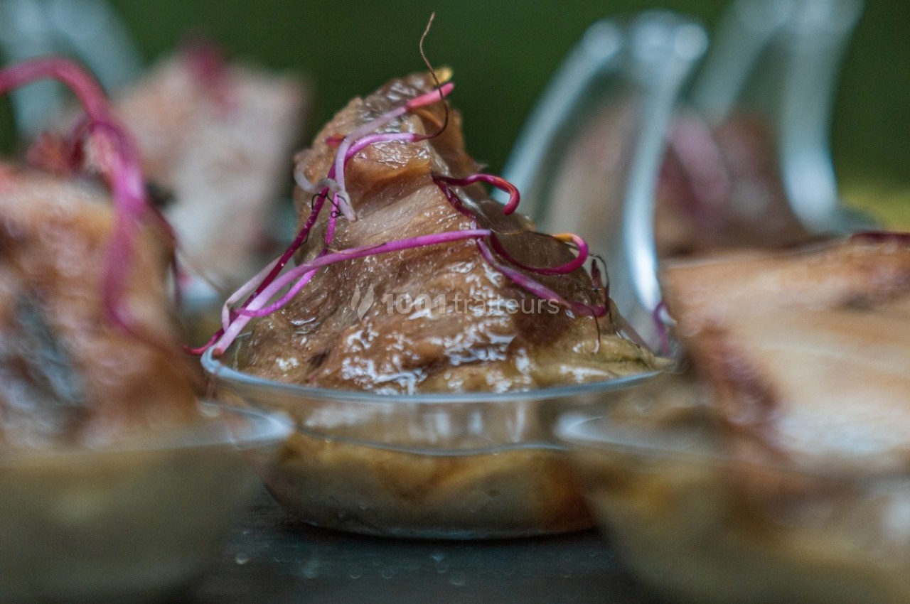 Portion de viande braisée servie dans une petite coupelle, garnie de pousses rouges.