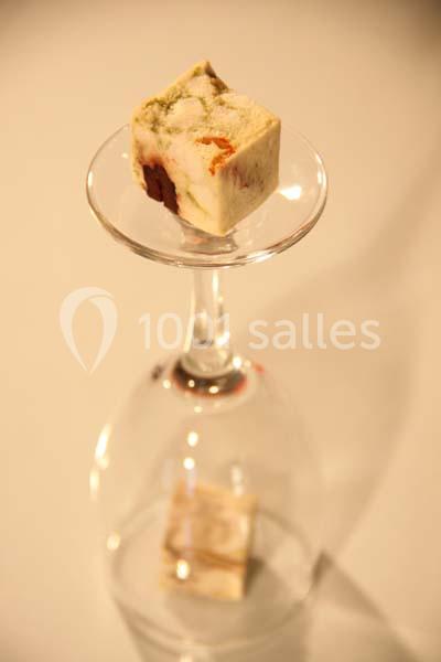 Cube de fromage aux herbes et légumes posé sur un verre à pied inversé, éclairé par une lumière douce.