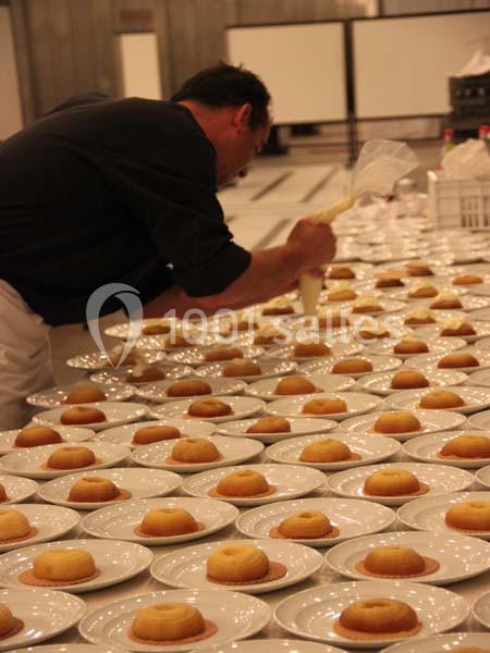 Un chef pâtissier décore des desserts alignés sur des assiettes blanches dans une grande cuisine.