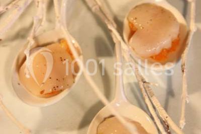 Table dressée avec nappes blanches, couverts, menus et bouquets de fleurs, entourée de chaises en bois dans une salle.