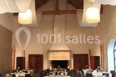 Table dressée avec nappes blanches, couverts, menus et bouquets de fleurs, entourée de chaises en bois dans une salle.