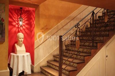 Table dressée avec nappes blanches, couverts, menus et bouquets de fleurs, entourée de chaises en bois dans une salle.