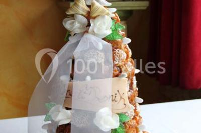 Table dressée avec nappes blanches, couverts, menus et bouquets de fleurs, entourée de chaises en bois dans une salle.