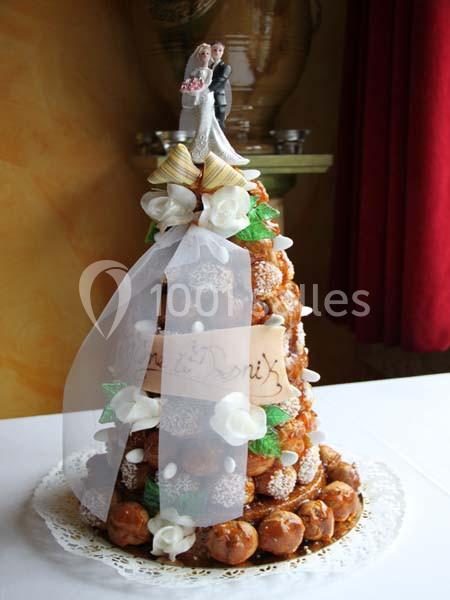 Pièce montée en choux décorée de fleurs en sucre, ruban blanc et figurine de mariés au sommet.