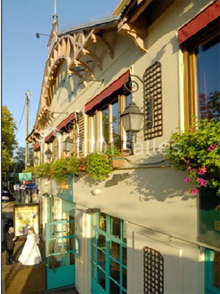 Façade d'un bâtiment ancien avec des balcons fleuris, des fenêtres à auvents rouges et une entrée vitrée.