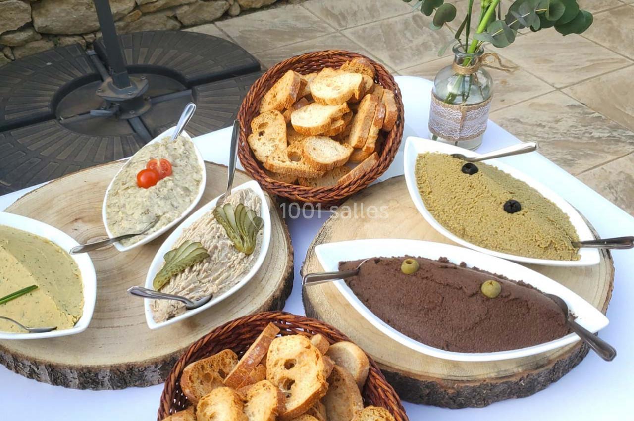 Assortiment de tartinades et de pain disposés sur des plateaux en bois, avec une décoration florale en arrière-plan.