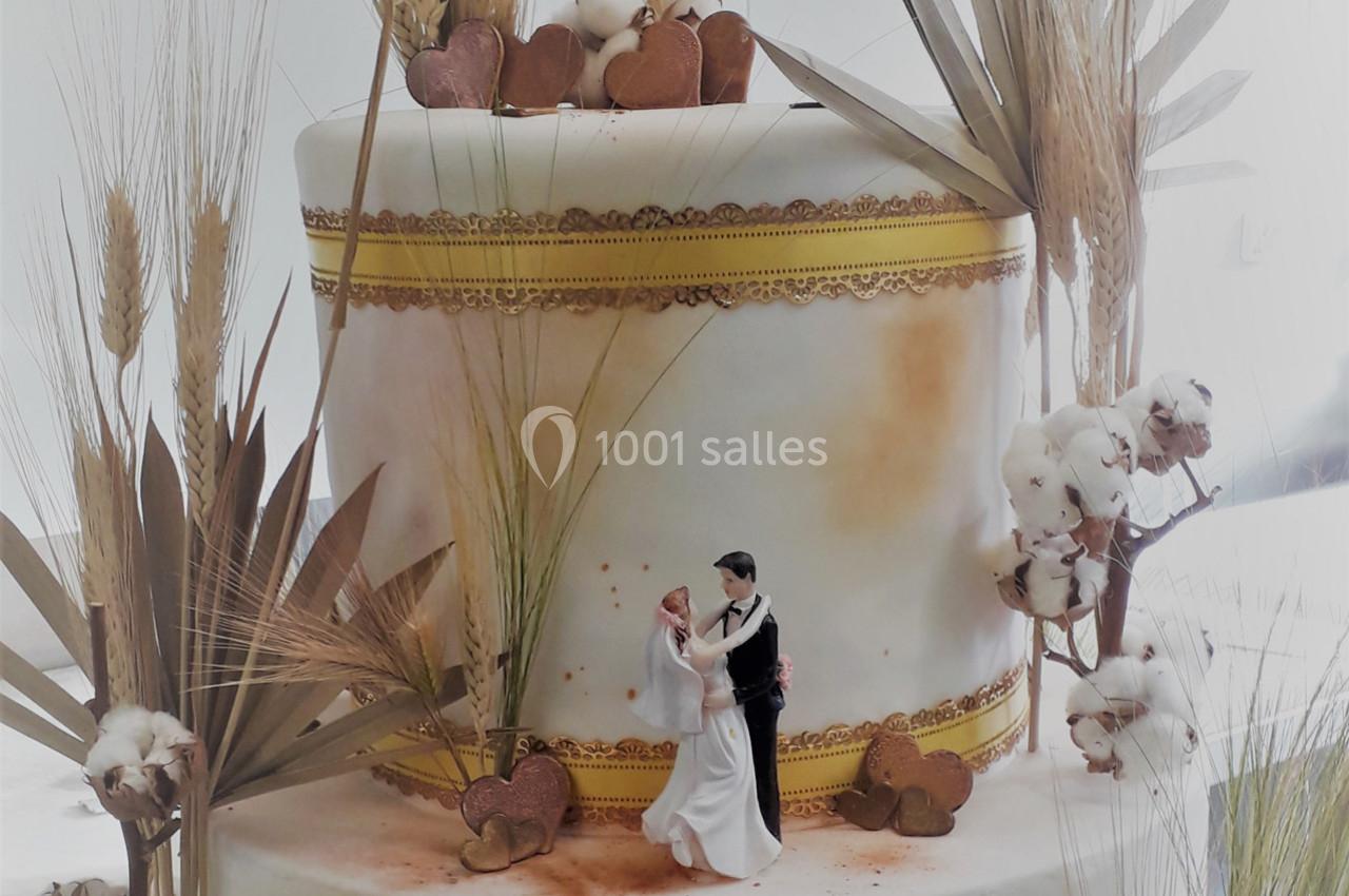 Gâteau de mariage décoré de fleurs séchées, épis de blé et figurines de mariés au sommet.