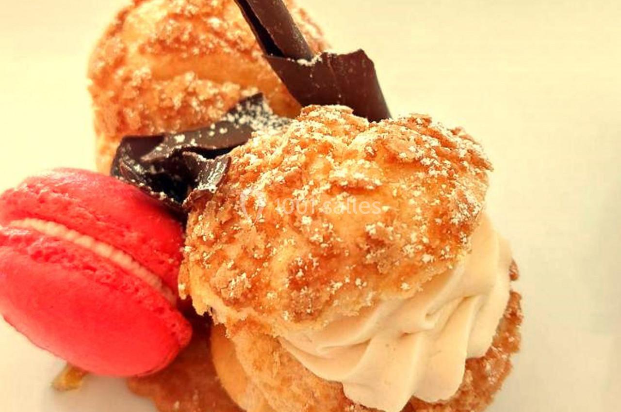 Deux choux garnis de crème, décorés de chocolat et accompagnés d'un macaron rose sur une assiette claire.