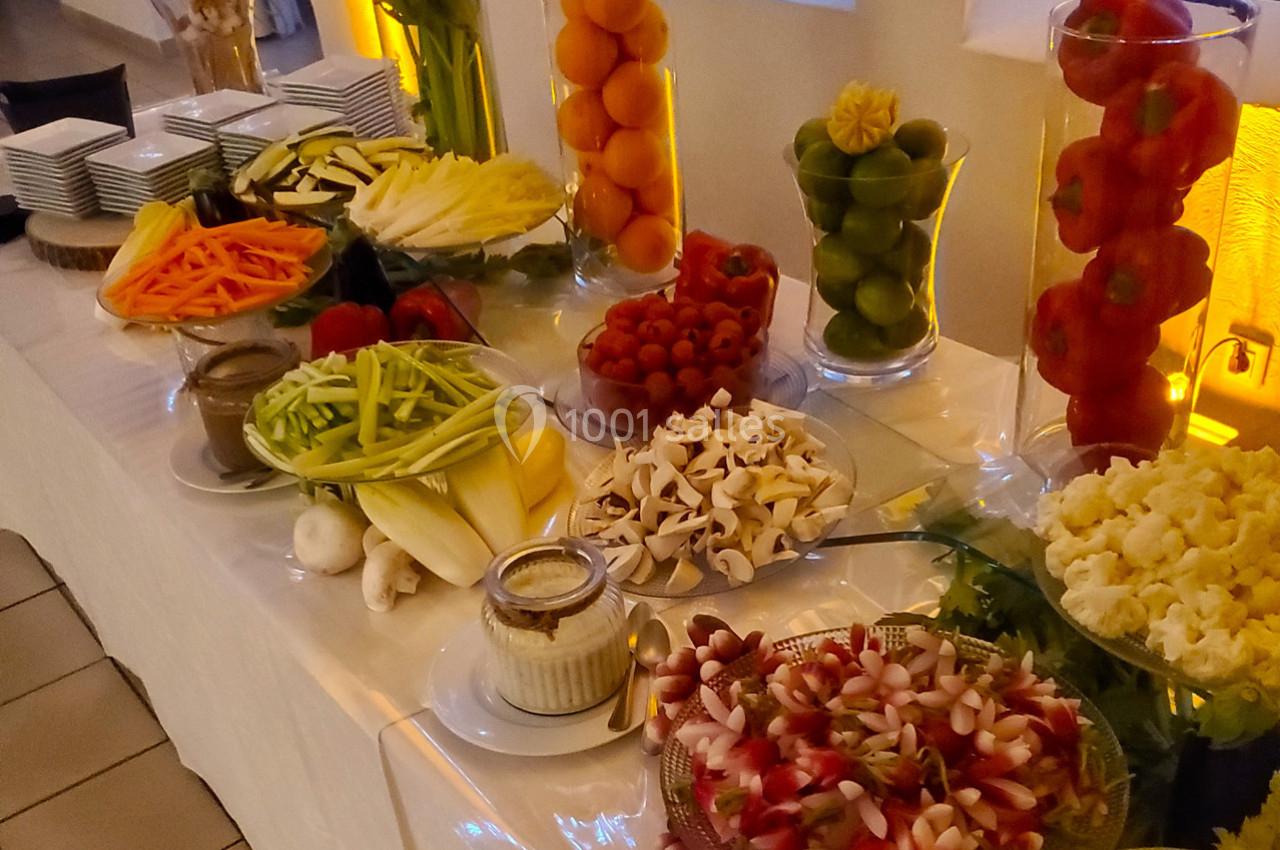 Buffet de légumes frais variés disposés sur une table, accompagnés de sauces et présentés dans des plats et des vases.