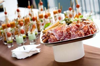 Une main coupe un rouleau de foie gras sur une planche en bois, entouré de figues et de tomates cerises.