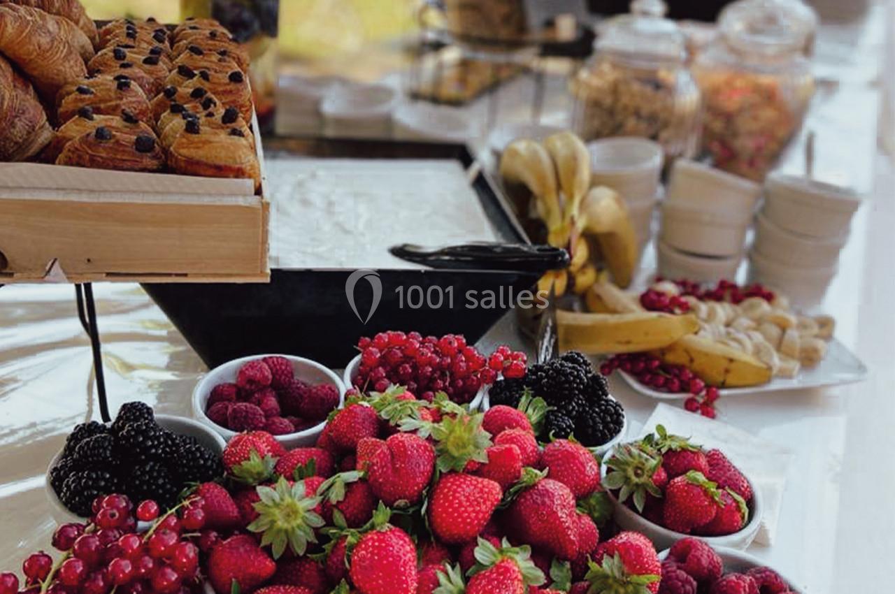 Table garnie de fruits rouges, croissants, bananes et céréales, disposés pour un buffet en plein air.