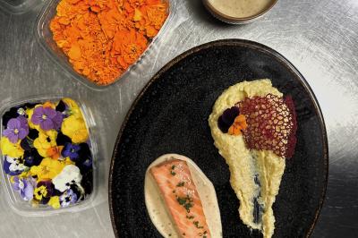 Une main coupe un rouleau de foie gras sur une planche en bois, entouré de figues et de tomates cerises.