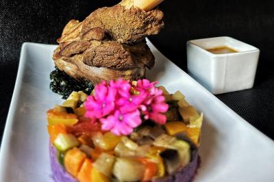 Une main coupe un rouleau de foie gras sur une planche en bois, entouré de figues et de tomates cerises.