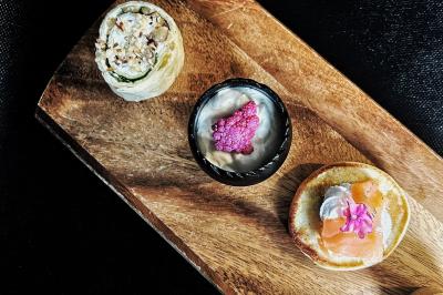 Une main coupe un rouleau de foie gras sur une planche en bois, entouré de figues et de tomates cerises.