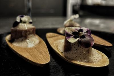Une main coupe un rouleau de foie gras sur une planche en bois, entouré de figues et de tomates cerises.