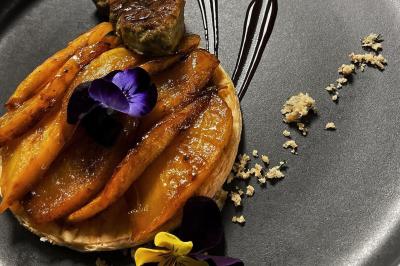 Une main coupe un rouleau de foie gras sur une planche en bois, entouré de figues et de tomates cerises.