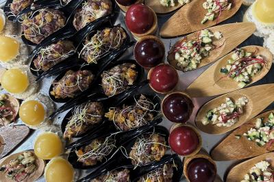 Miniature Traiteur Chaponost (Rhône) - Jacques Lafargue Traiteur #4 Une main coupe un rouleau de foie gras sur une planche en bois, entouré de figues et de tomates cerises.