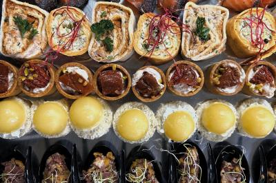 Miniature Traiteur Chaponost (Rhône) - Jacques Lafargue Traiteur #5 Une main coupe un rouleau de foie gras sur une planche en bois, entouré de figues et de tomates cerises.