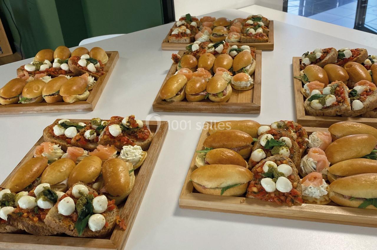 Plateaux en bois garnis de mini-sandwichs, bruschettas et bouchées variées disposés sur une table blanche.
