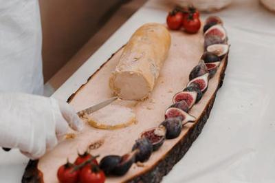 Miniature Traiteur Chaponost (Rhône) - Jacques Lafargue Traiteur #32 Une main coupe un rouleau de foie gras sur une planche en bois, entouré de figues et de tomates cerises.