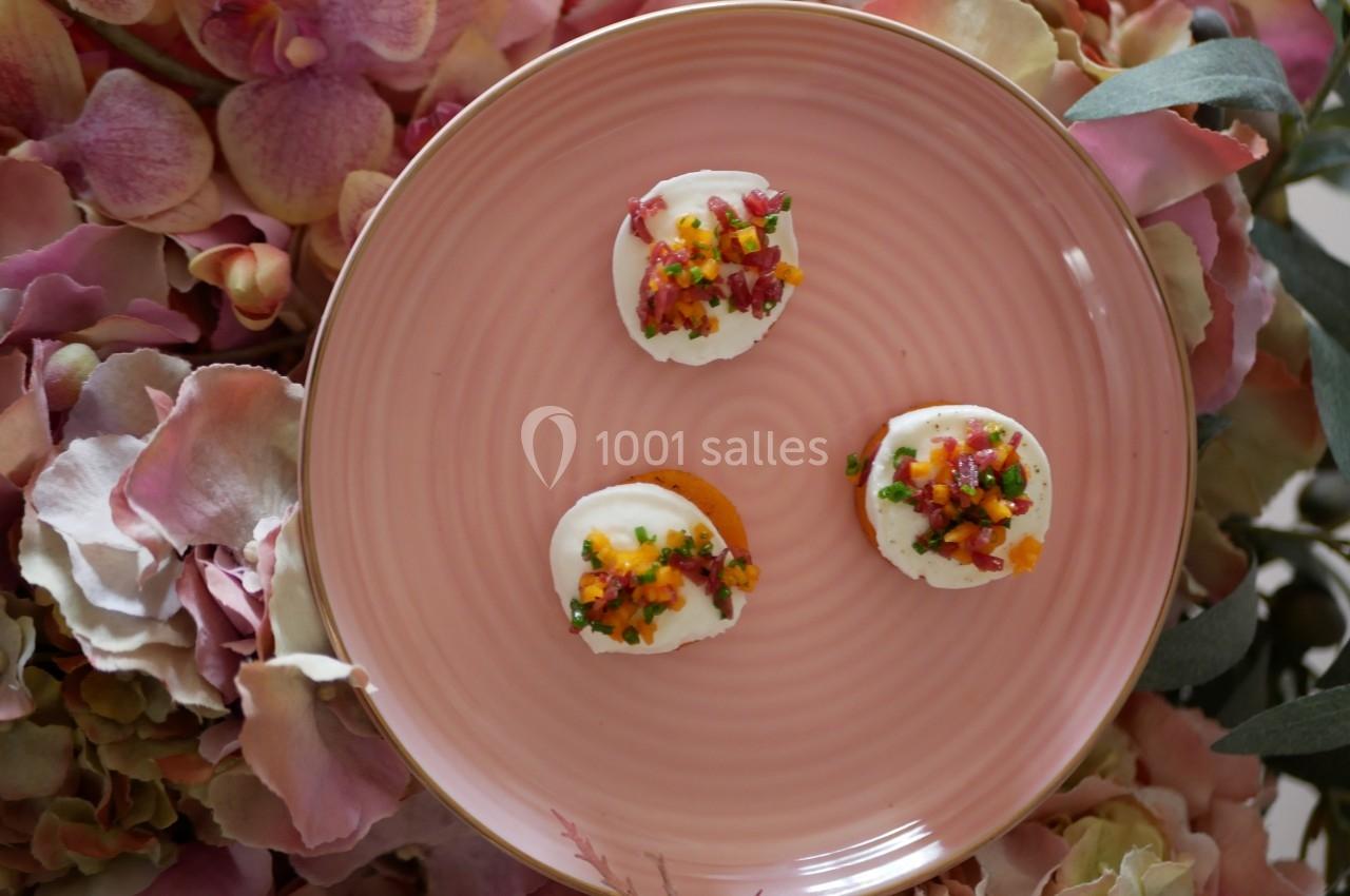 Assiette rose contenant trois amuse-bouches colorés, posée sur un fond de fleurs pastel.