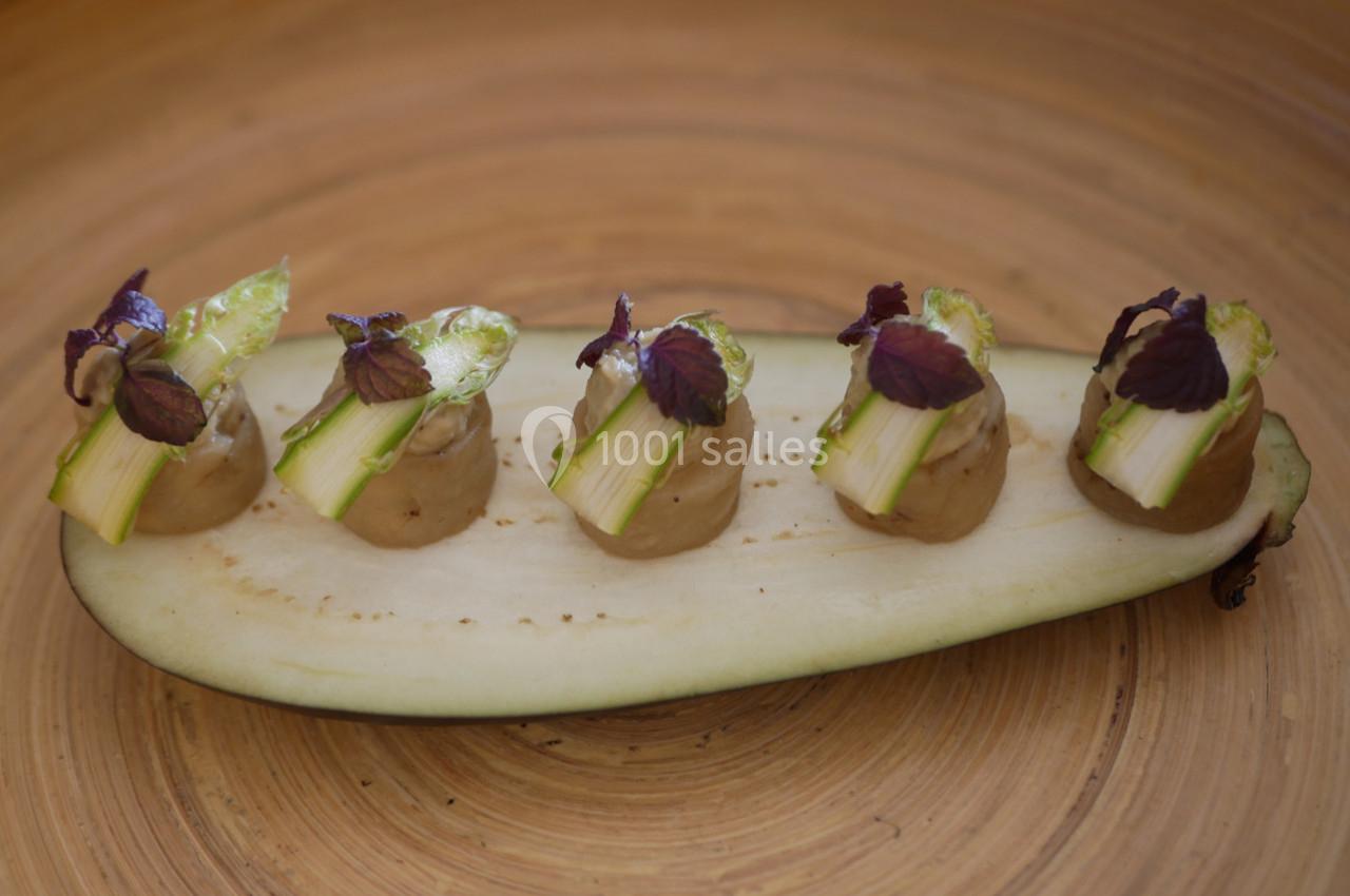 Tranche d'aubergine garnie de purée, morceaux d'asperges et feuilles violettes sur un fond en bois.