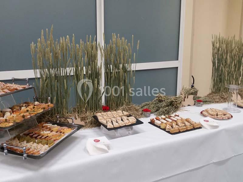 Buffet avec des plateaux de petits fours et pâtisseries, décoré de gerbes de blé sur une nappe blanche.