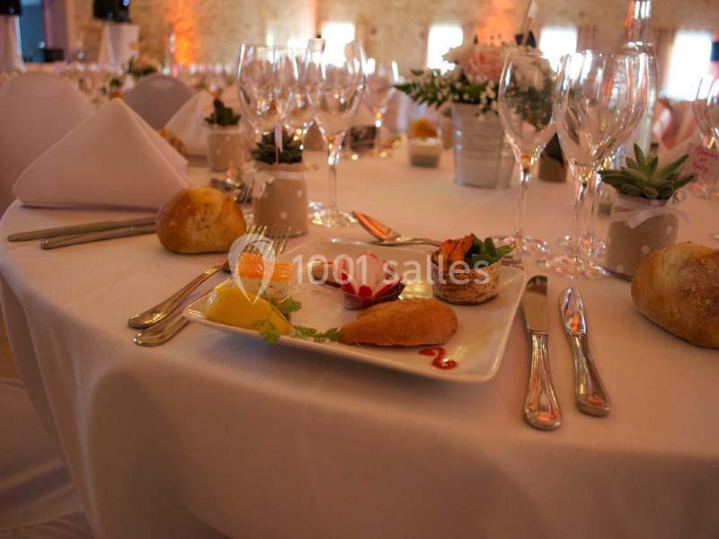 Table dressée avec une assiette d'entrée raffinée, couverts, verres à pied et décoration florale dans une salle éclairée.