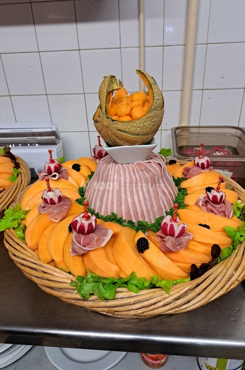 Plateau de présentation avec tranches de melon, jambon cru, décorations de fruits et billes de melon en centre.