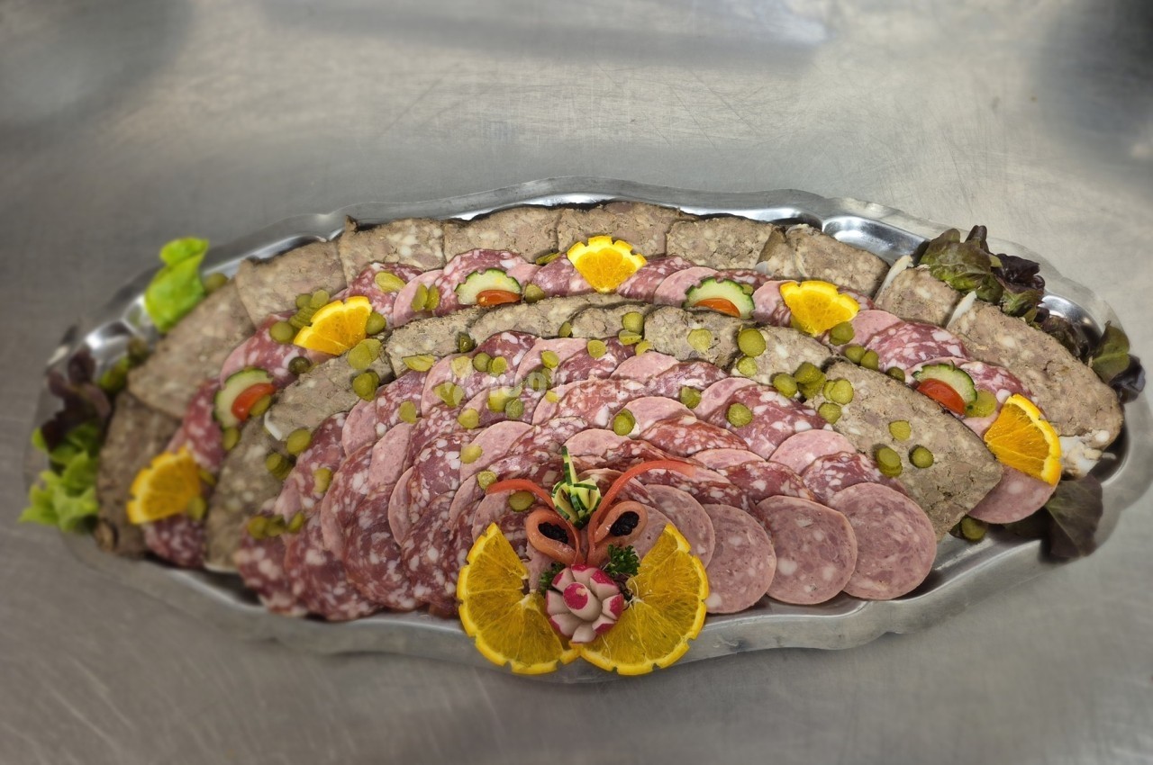 Plateau de charcuterie variée avec tranches de saucisson, cornichons, rondelles d'orange et décoration centrale.