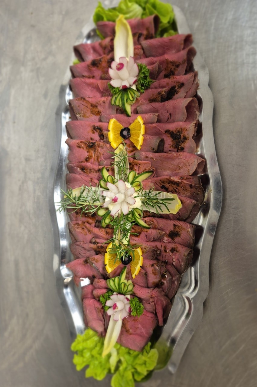Plateau de tranches de viande froide garnies de légumes, herbes, rondelles d'orange et décorations florales.
