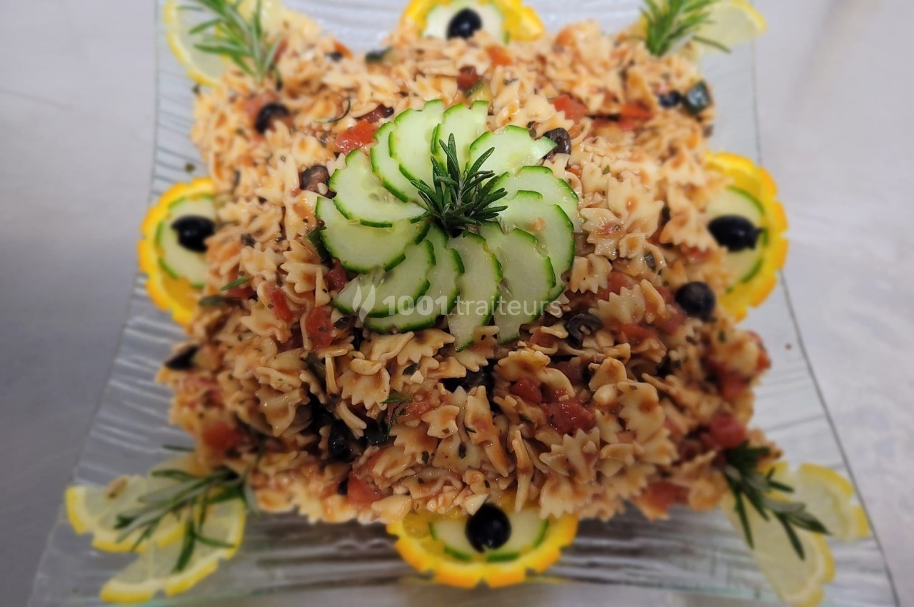 Salade de pâtes farfalle garnie de rondelles de concombre, olives noires, tomates et décorée de tranches de citron.