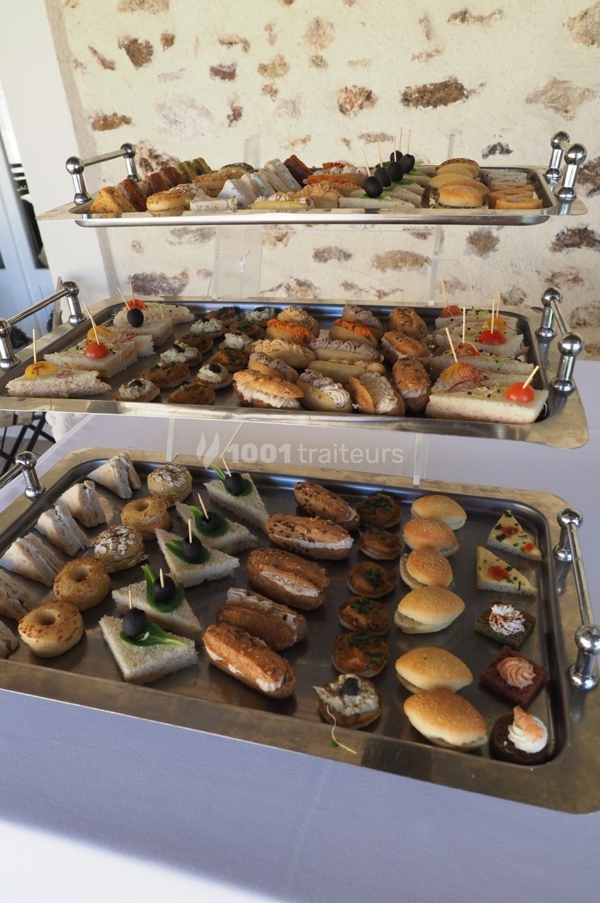 Plateaux de petits fours variés, incluant canapés, mini-sandwichs et pâtisseries, présentés sur une table blanche.