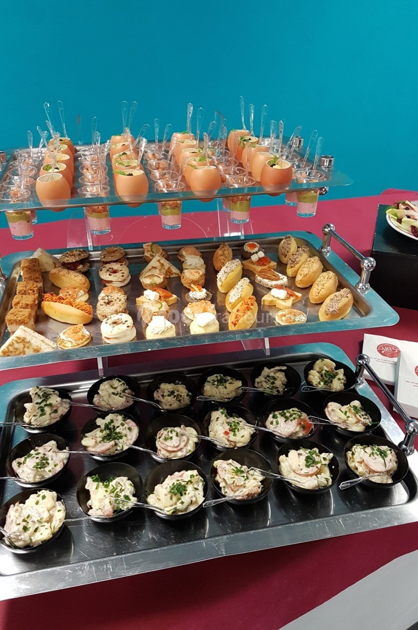 Plateau de verrines, bouchées salées et salades individuelles disposés sur une table avec nappe rouge.
