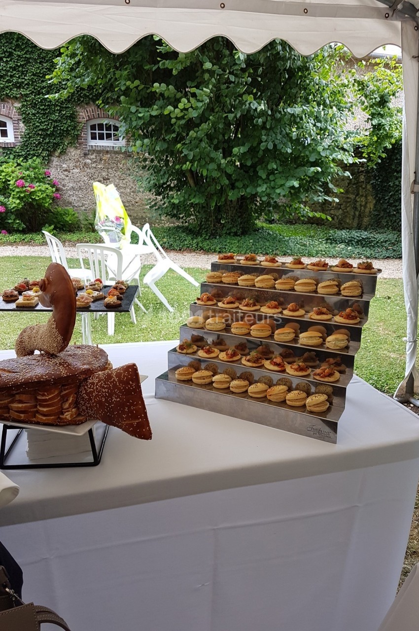 Plateau de petits fours et pâtisseries disposés sur une table sous une tente, dans un jardin verdoyant.